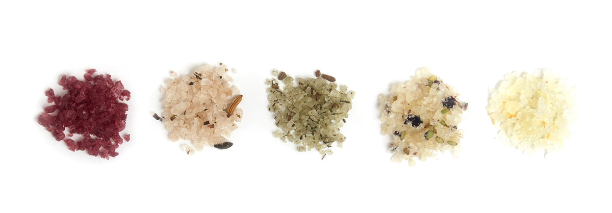 Five small piles of different flavored and infused Amagansett Sea Salt blends on a white background